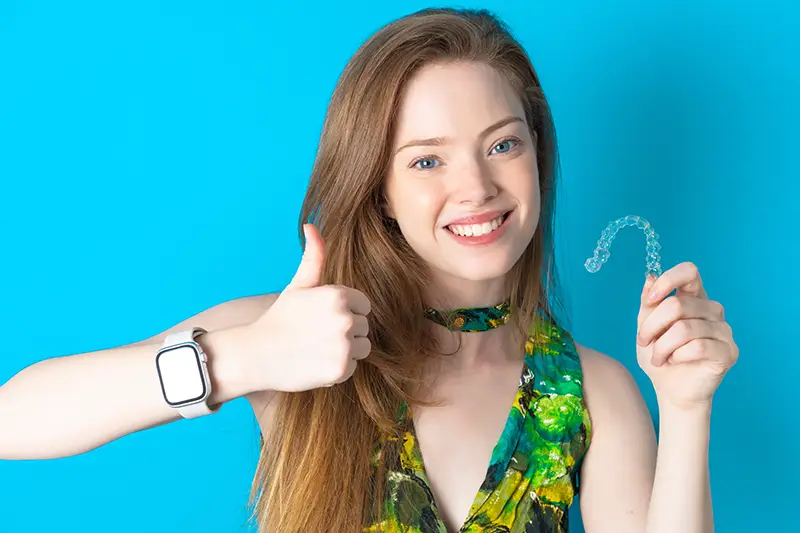 Invisalign for Teens - Ovation Orthodontics young girl with long hair smiling and giving thumbs up while holding invisalign aligner