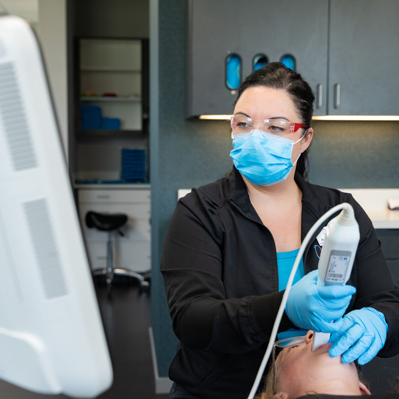 Ovation Orthodontics team member in a face mask scanning a patient's teeth with a digital intraoral scanner