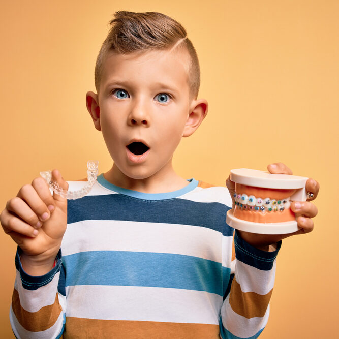 young boy holding aligners and braces typodont